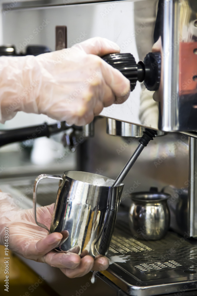 A barista at a cafe churns milk in a metal jug using a caper of professional coffee machine. Coffee house concept. The process of making cappuccino or latte A barista at a cafe churns milk in a metal jug using a caper of professional coffee machine. Coffee house concept. The process of making cappuccino or latte