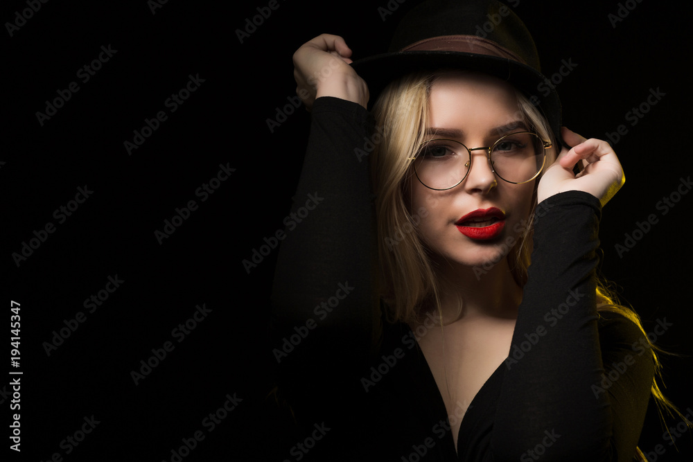 Lovely young woman wearing brown hat and glasses, posing at black background Lovely young woman wearing brown hat and glasses, posing at black background