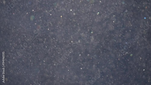 Sunny snowstorm with shallow focus and sparkling colorful snowflakes on gray background. Abstract glittering backdrop in slow motion. Excellent meditative and relax intro with blinking gleams.
