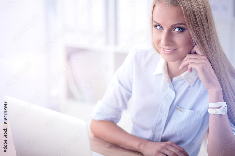 Attractive businesswoman sitting on a desk with laptop in the office Attractive businesswoman sitting on a desk with laptop in the office