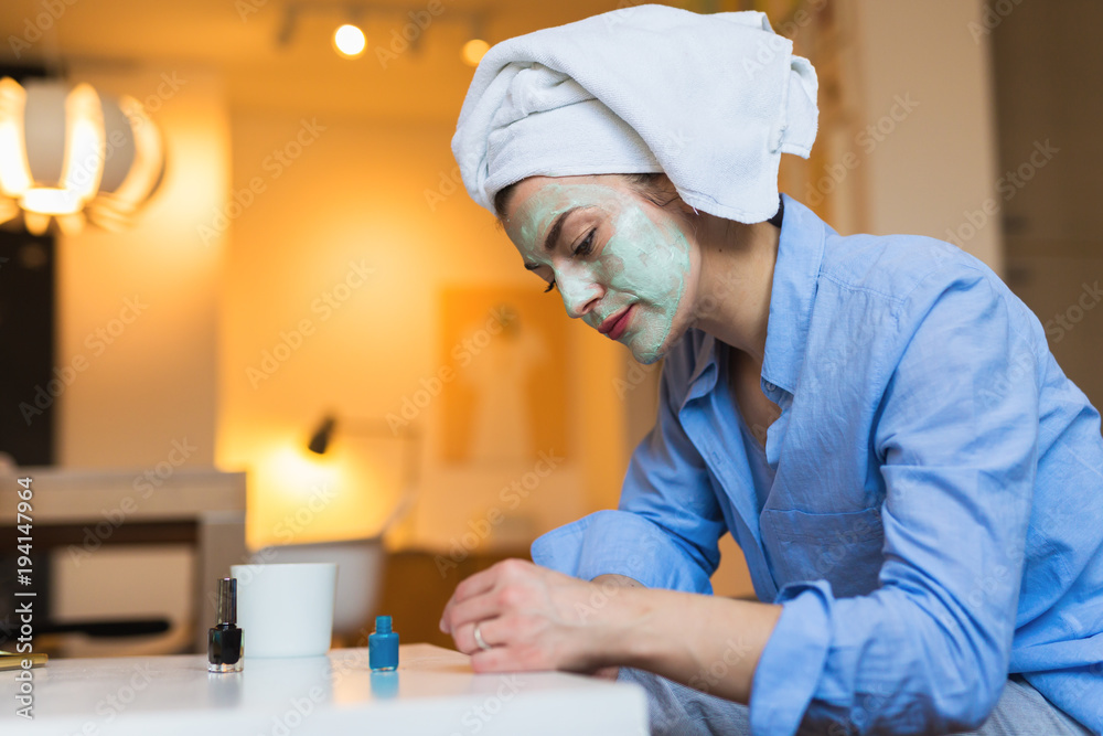Woman with cosmetic face mask applied polish nails at her home