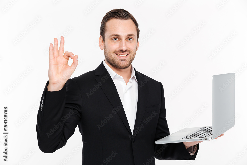 Smiling young businessman showing okay gesture using laptop. Smiling young businessman showing okay gesture using laptop.