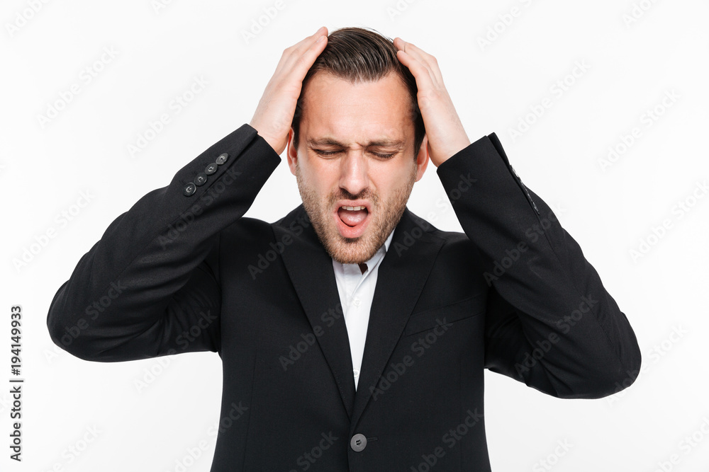 Horizontal portrait of tense man in suit grabbing his head being stressed and thinking about solution of problem, isolated over white background Horizontal portrait of tense man in suit grabbing his head being stressed and thinking about solution of problem, isolated over white background