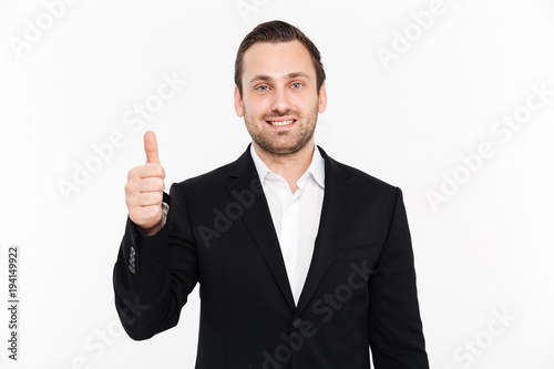 Portrait of happy entrepreneur wearing black formal suit and showing thumb up on camera with smile, isolated over white background