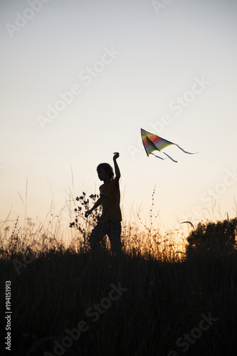 boy playing kite on summer sunset meadow silhouetted