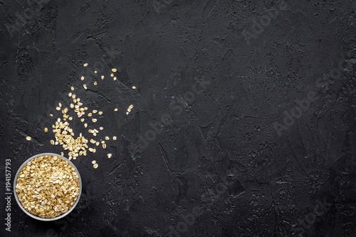 Uncooked oatmeal in bowl on black background top view copy space