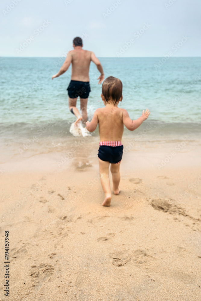 Back view of little child and father running together on wet sandy beach. Back view of little child and father running together on wet sandy beach.