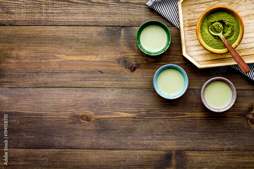 Japanise tea ceremony with matcha tea. Bowl with powder and cups with beverage on tablecloth on dark wooden background top view copy space