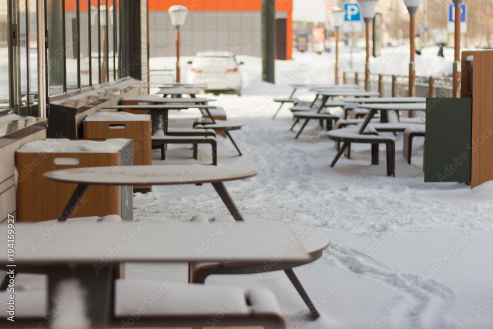 summer cafe on the veranda in winter, tables and benches are covered with snow