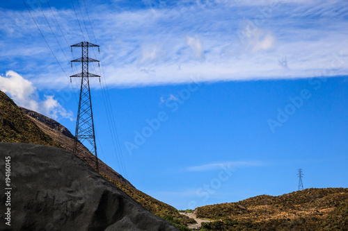High voltage electricity distribution system power metal frame structure tower in the landscape rural area with blue sky background and copy space.