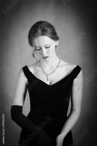 Girl in evening dress taking off long gloves. Black and white portrait in studio