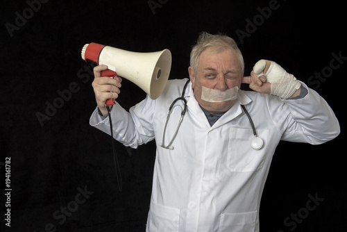 Mature doctor with tape across his mouth and listening to a message through a megaphone   photo