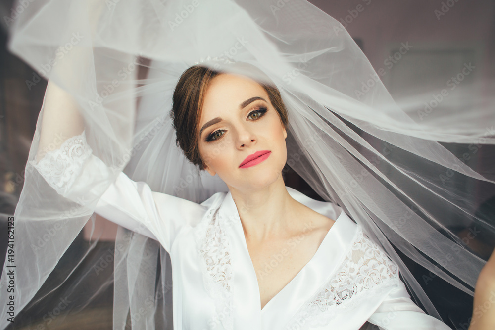 Beautiful bride stands hidden under the veil in a bright room