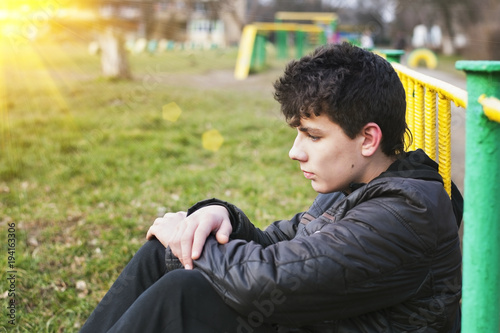 A teenager with a sad face sits on the grass and dreams of a better life