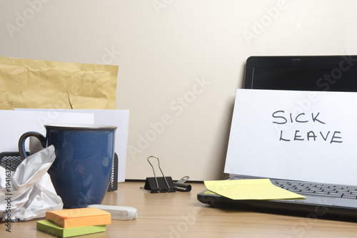 Sick leave message left on a messy office desk  photo