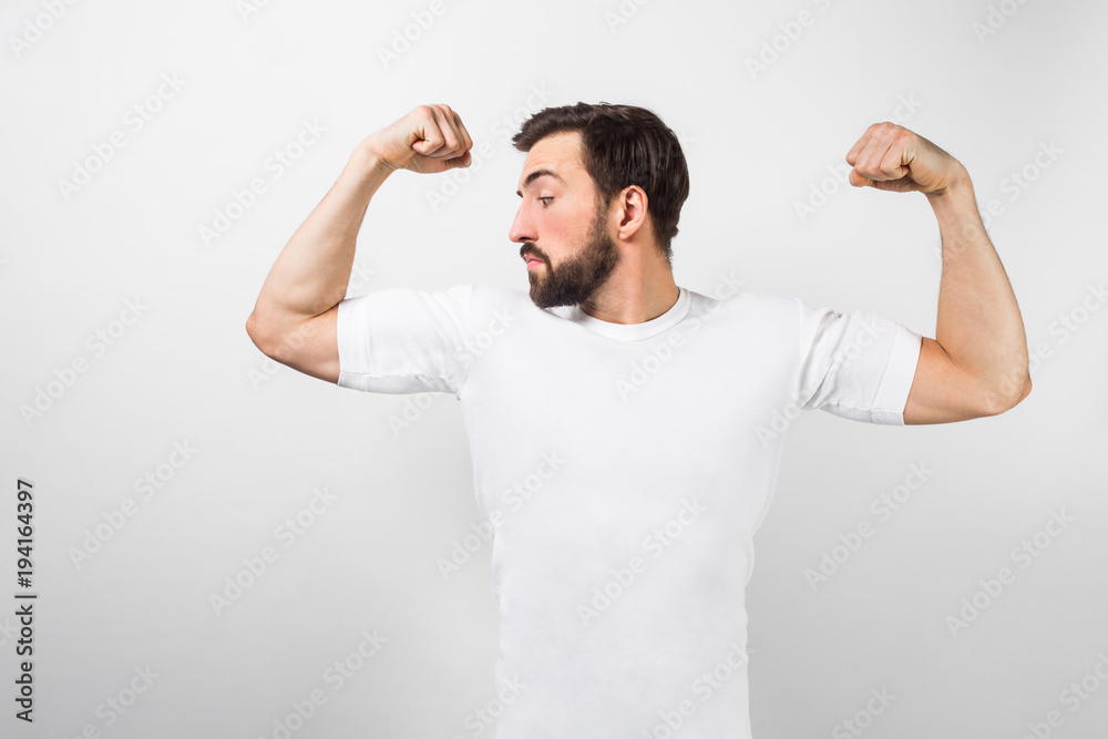 A handsome confident young man standing and showing big muscles on his  hands. He is looking