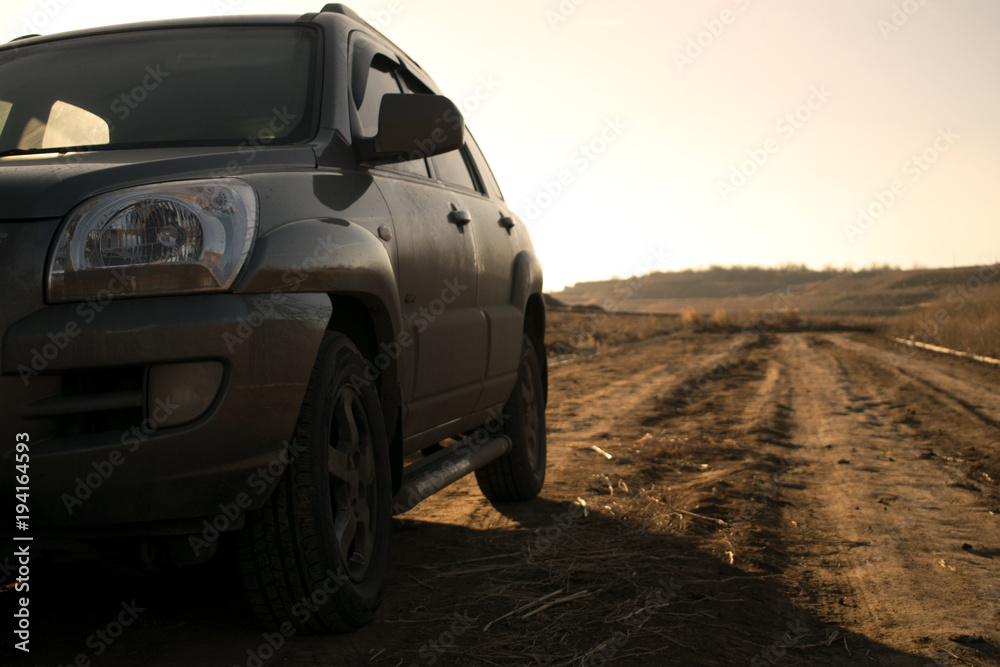 SUV in the field at sunset, car and a road, headlight, warm, dusty evening