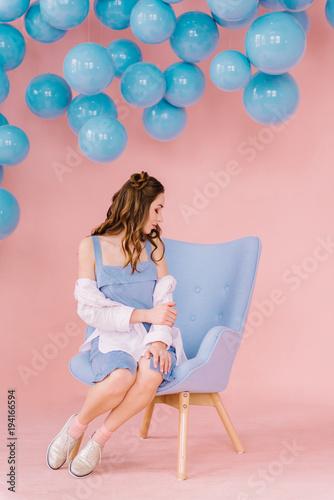 Beautiful girl in a blue dress in a pink room with blue balls and a blue armchair © Ilya.K