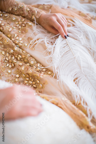 Female hand holding big long white feather. Beautiful dress decorated with jewels