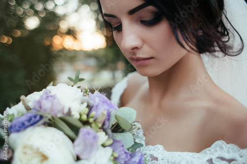 Stunning young bride stands in the forest with tall trees and morning sunshine