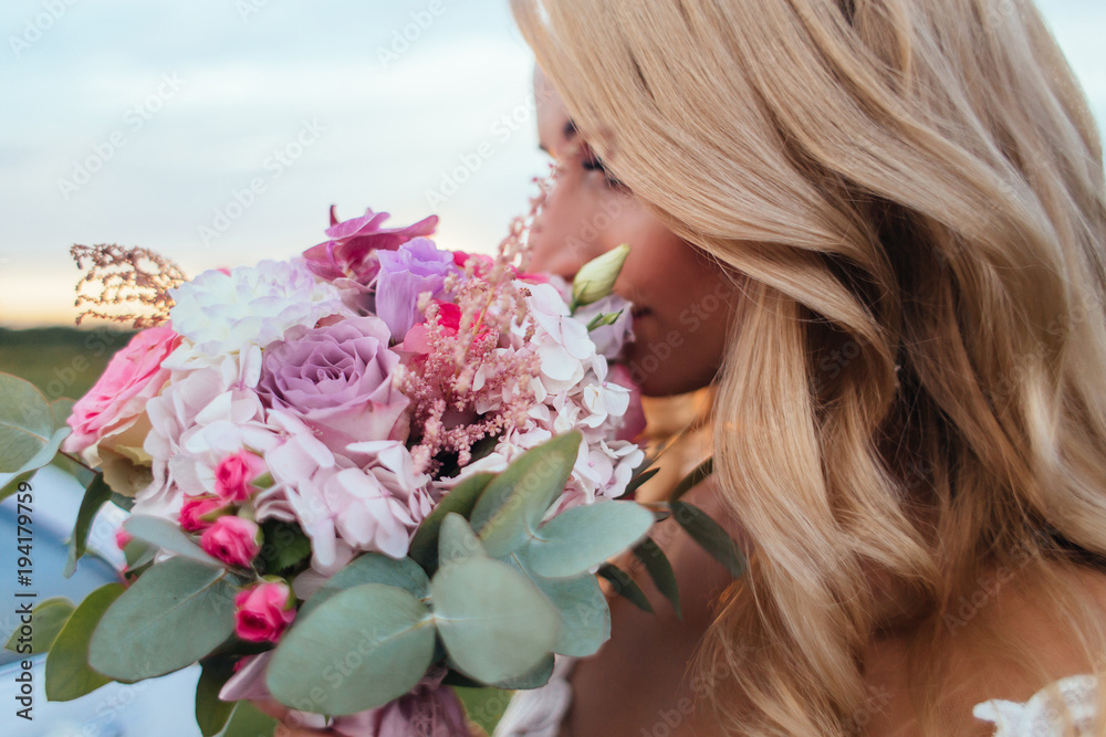Blonde bride holds pink wedding bouquet before her face