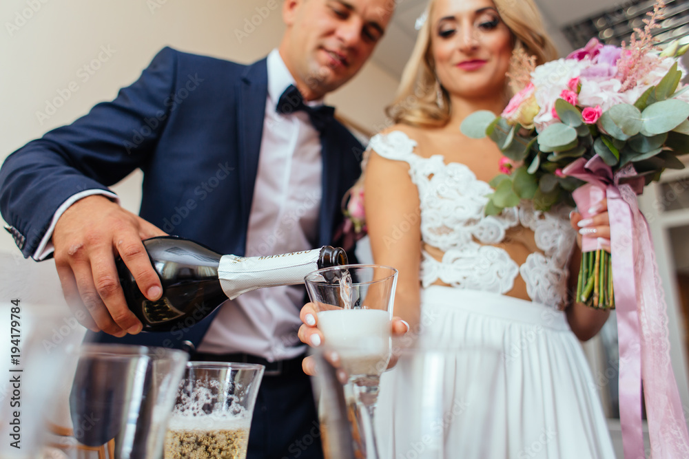 Groom pours champagne in the glasses standing with a bride Groom pours champagne in the glasses standing with a bride