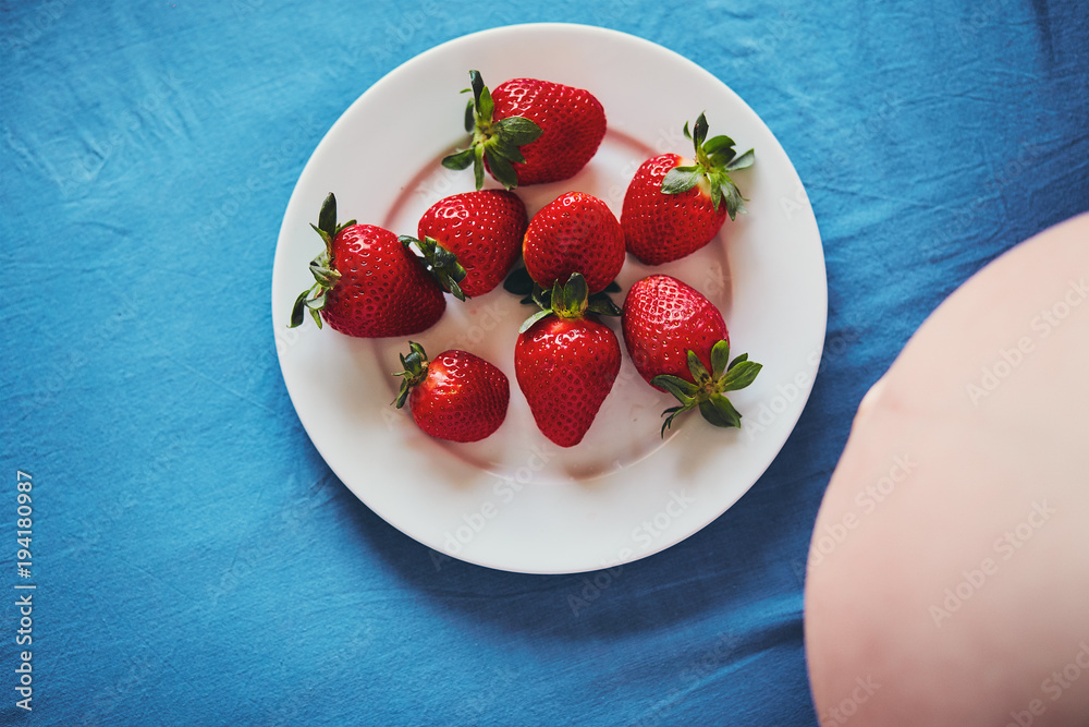 The belly of a pregnant woman sitting on a bed with a blue sheet and a