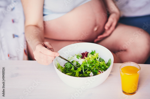 White bowl with green and red salad. Orange, pumpkin, carrot, mango juice on a wooden table. Healthy food for pregnancy. Diet for pregnant women and girls. The concept of healthy eating and pregnancy.