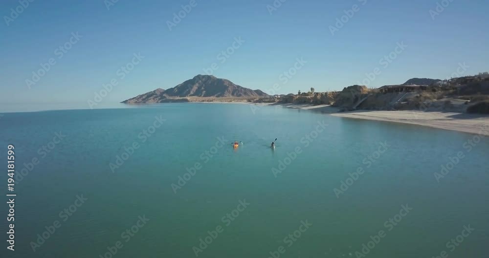 Aerial camera moves forward and over a couple paddling kayaks with a mountain in the distance. Aerial camera moves forward and over a couple paddling kayaks with a mountain in the distance.