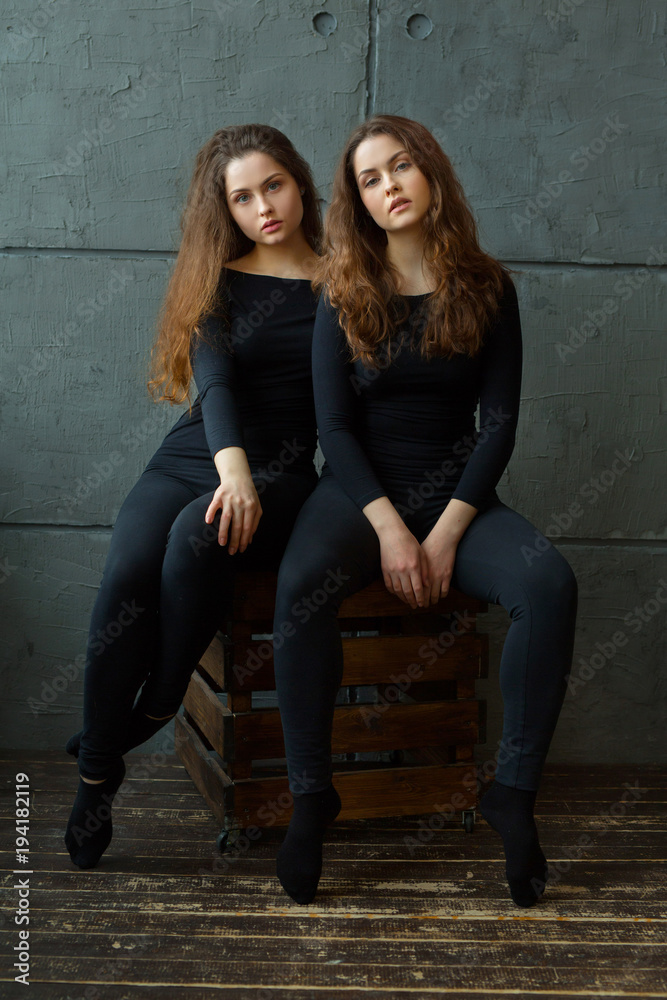 portrait of two beautiful young girls of twin sisters with flowing hair against the gray wall in the interior
