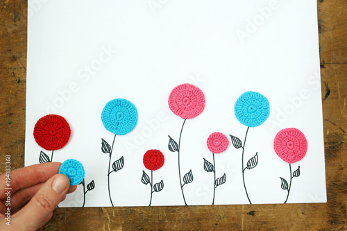 hand lays knitted flowers on a white background. view from above. children's background