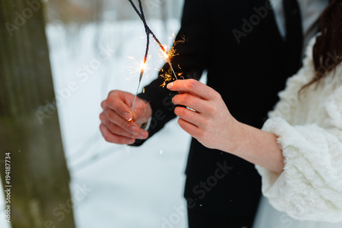 Young couple with Bengali lights in winter forest. Hands with Bengali lights. Happy festive couple with lit sparklers celebrating Christmas outdoors. People, winter, holidays, the concept of outdoors