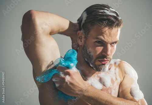 Spa and beauty, relax and hygiene, healthcare - handsome man washing with sponge in shower. Attractive stylish bearded macho model with fashion hair takes shower with soap sponge. Copy space.