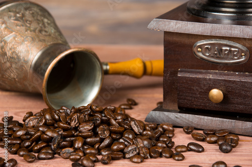 Vintage coffee grinder, turk copper coffee pot and coffee beans on brown wooden background.
