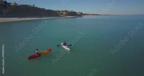 Aerial view of a couple kayaking in a sea toward a mountain in the distance.