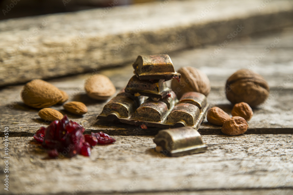 Pieces of black, chocolate with cranberry , nuts and almond on wood background Pieces of black, chocolate with cranberry , nuts and almond on wood background