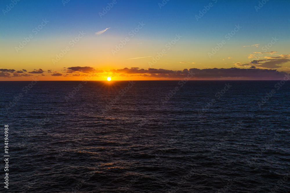 Sun setting on horizon between ocean and sky Sun setting on horizon between ocean and sky