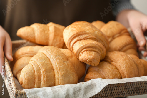 Woman holding wicker tray with delicious croissants, closeup
