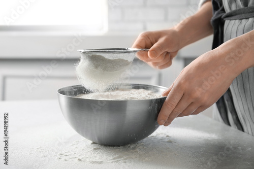 Woman sifting flour into bowl on table