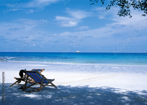 Two wooden chaise-longues on white tropical beach against quiet blue sea