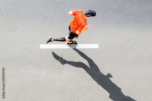 Single runner in sportswear against asphalt road with marking, top view
