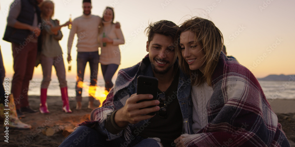 Obraz premium Couple enjoying bonfire with friends on beach