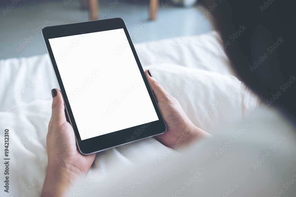 Mockup image of woman's hands holding black tablet pc with blank desktop white screen while sitting on a white bed