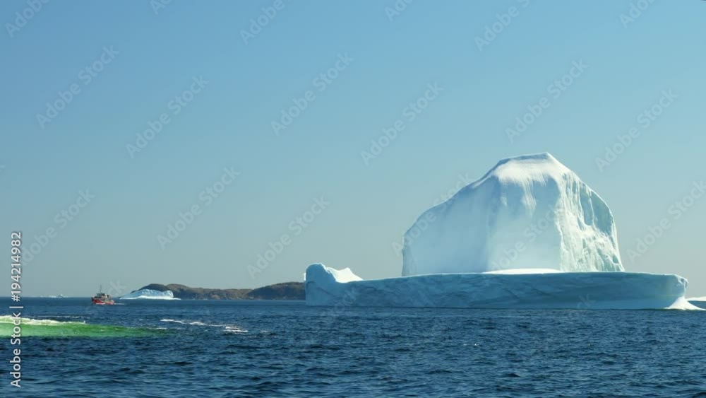 Boat by a massive ice berg floating off a coast in a cold sea Boat by a massive ice berg floating off a coast in a cold sea