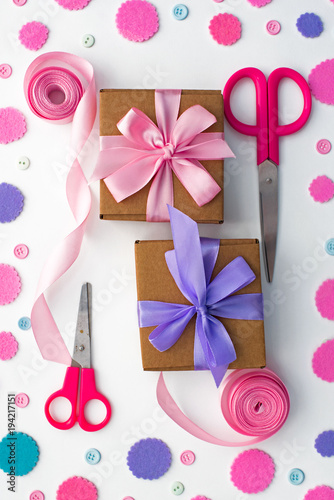 Two holiday gift boxes are tied with satin ribbon on background with colorful confetti.