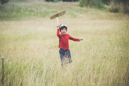 child playing cardboard airplane in the grass field
