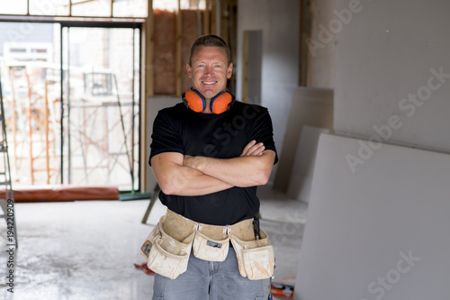 attractive and confident constructor carpenter or builder man with ear protection gear working happy at industrial construction site photo