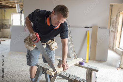 attractive and confident constructor carpenter or builder man working cutting wood with manual saw in industrial construction job concept © Wordley Calvo Stock