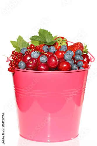 Berry season.bright pink bucket with berries of strawberries, blueberries, cherries, red currants on white background. Harvest of berries. Delicious ripe berries in a pink bucket