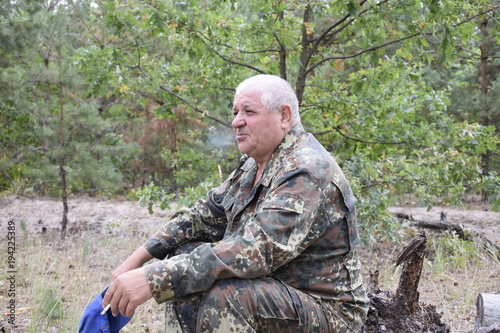 задумчивый кавказский старик отдыхая в лесу курит сигарету